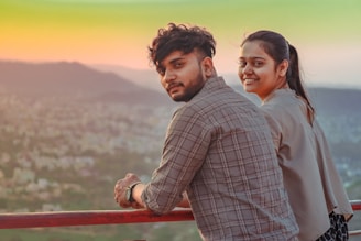 A smiling couple enjoying a scenic view from their hotel balcony at sunset.