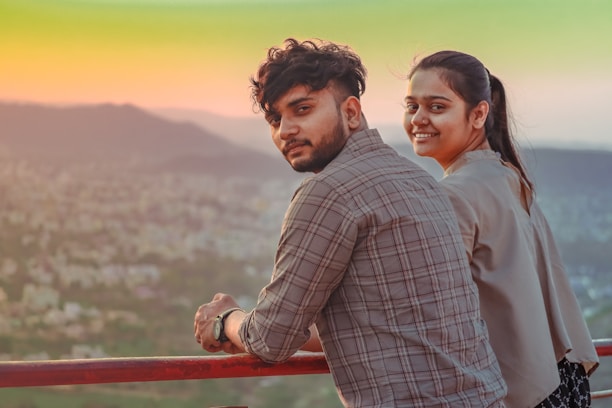 A smiling couple enjoying a scenic view from their hotel balcony at sunset.