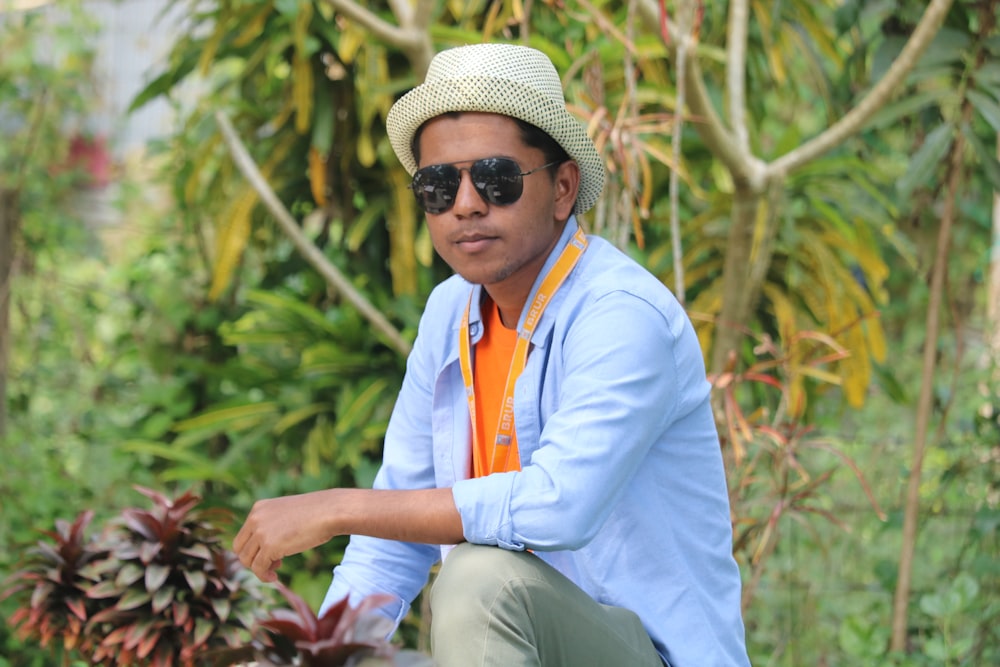 a man wearing a hat and sunglasses crouching down