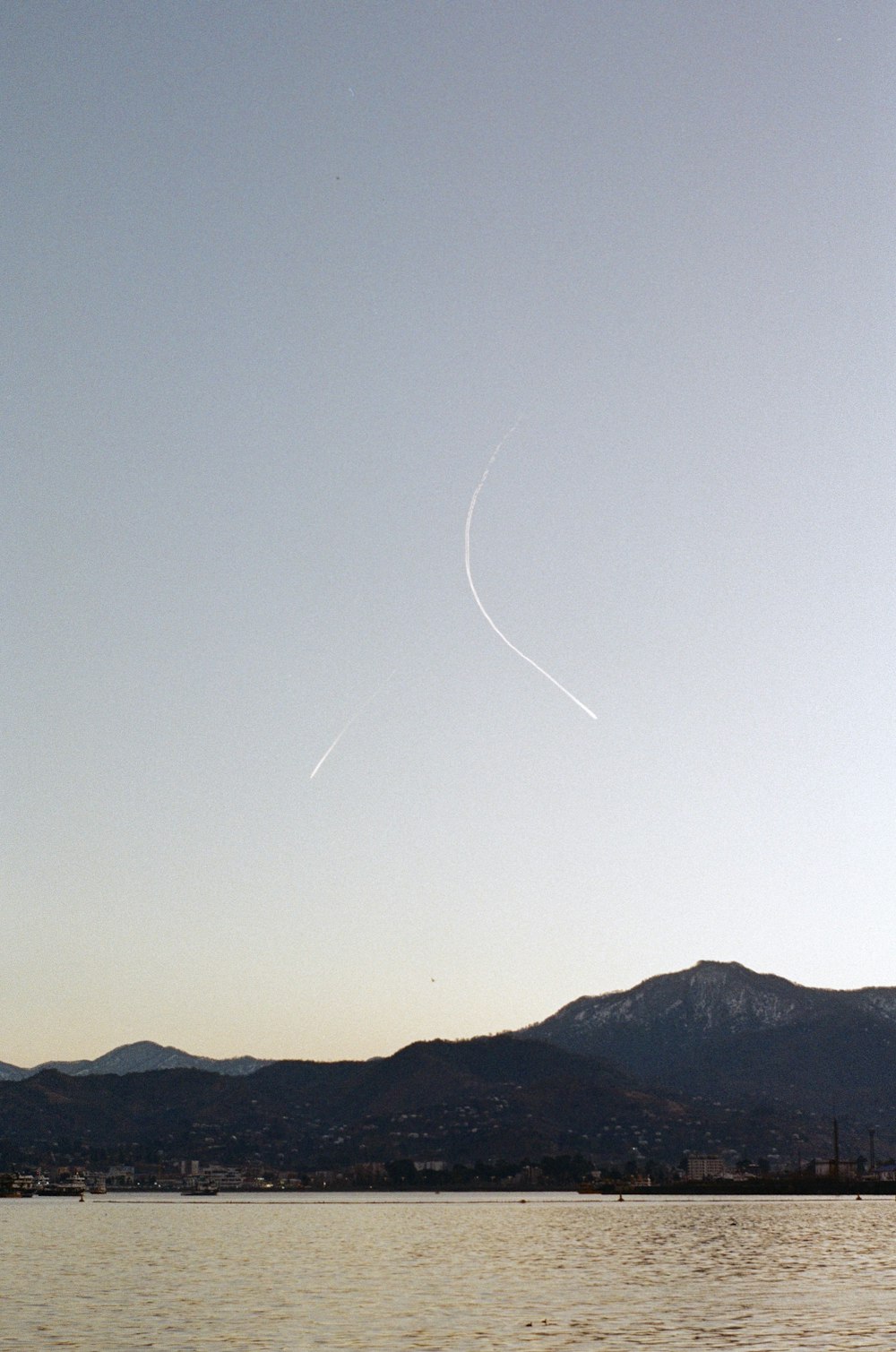 a plane flying over a body of water with mountains in the background