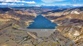Aerial shot of a water reservoir surrounded by green vegetation under a clear blue sky.