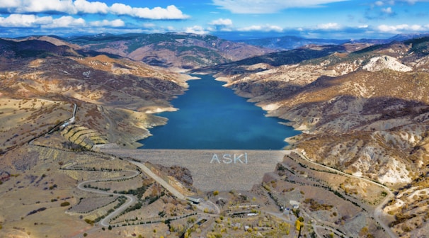 Aerial shot of a water reservoir surrounded by green vegetation under a clear blue sky.