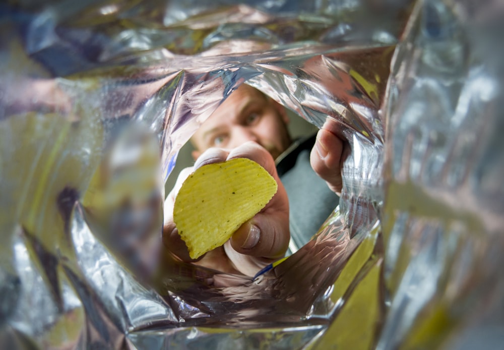 a man holding a cell phone and a potato chip in his hand