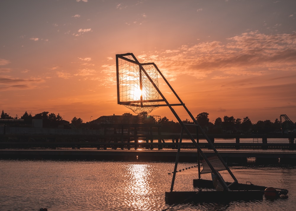 a basketball hoop in the water at sunset