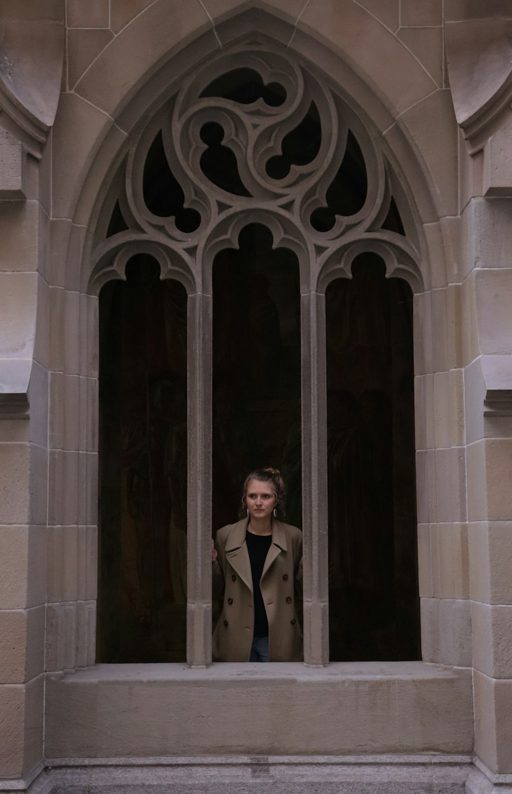 a woman in a trench coat looking out of a window