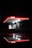 A brightly illuminated gas station canopy with the red Avia logo is set against a dark night background. The structure is reflected on a wet surface, creating a mirror image. Underneath the canopy, a person stands near the gas pumps, partially silhouetted by the lights.