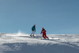 A group of skiers wearing advanced protective gear, preparing for a mountain descent under clear blue skies.