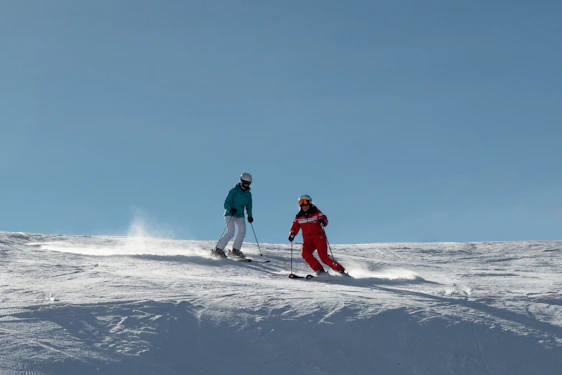 A group of skiers wearing advanced protective gear, preparing for a mountain descent under clear blue skies.