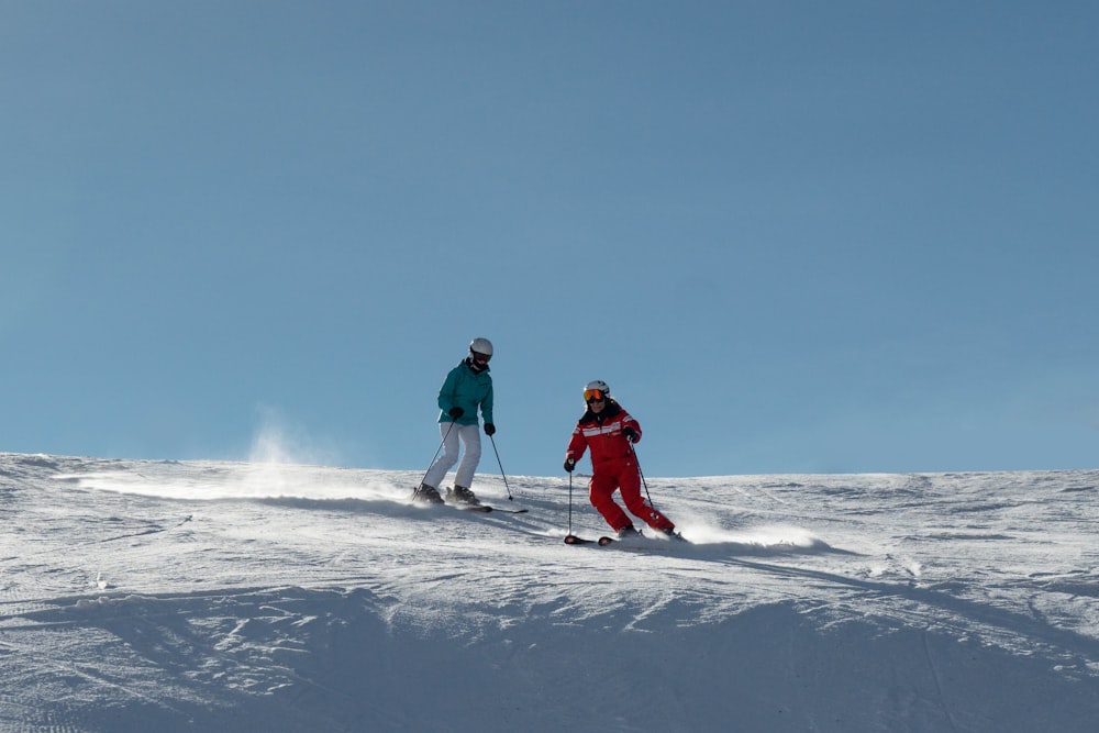 a couple of people riding skis down a snow covered slope