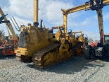 A lineup of heavy construction machinery, including large bulldozers and other vehicles, set on a gravel surface. The equipment features prominent treads and metal arms, indicating their use for construction and heavy-duty tasks.