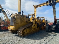 A lineup of heavy construction machinery, including large bulldozers and other vehicles, set on a gravel surface. The equipment features prominent treads and metal arms, indicating their use for construction and heavy-duty tasks.
