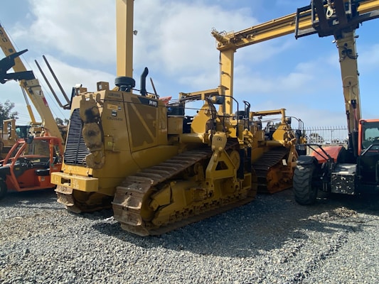 A lineup of heavy construction machinery, including large bulldozers and other vehicles, set on a gravel surface. The equipment features prominent treads and metal arms, indicating their use for construction and heavy-duty tasks.