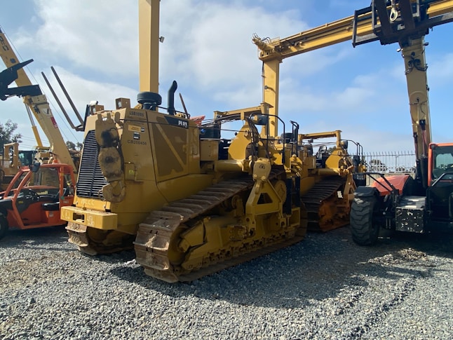 A lineup of heavy construction machinery, including large bulldozers and other vehicles, set on a gravel surface. The equipment features prominent treads and metal arms, indicating their use for construction and heavy-duty tasks.