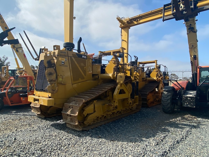 A lineup of heavy construction machinery, including large bulldozers and other vehicles, set on a gravel surface. The equipment features prominent treads and metal arms, indicating their use for construction and heavy-duty tasks.