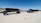 A large dump trailer with multiple wheels sits on a sandy desert landscape under a clear blue sky. Mountains are visible in the background, and the land is barren with sparse vegetation.