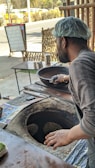 A chef in traditional attire preparing fresh naan bread in a tandoor oven.