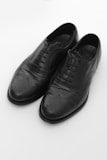 A pair of black leather dress shoes with intricate brogue detailing on the toe and sides, featuring laces and a polished finish.