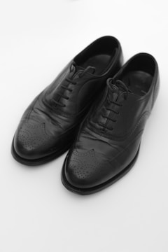A pair of black leather dress shoes with intricate brogue detailing on the toe and sides, featuring laces and a polished finish.
