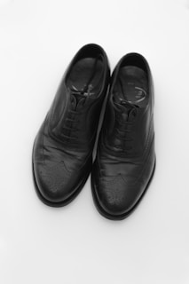 A pair of black leather dress shoes with intricate brogue detailing, placed side by side on a plain white background.