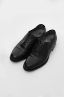 Formal shoes polished to a shine, displayed on a minimalist black surface.