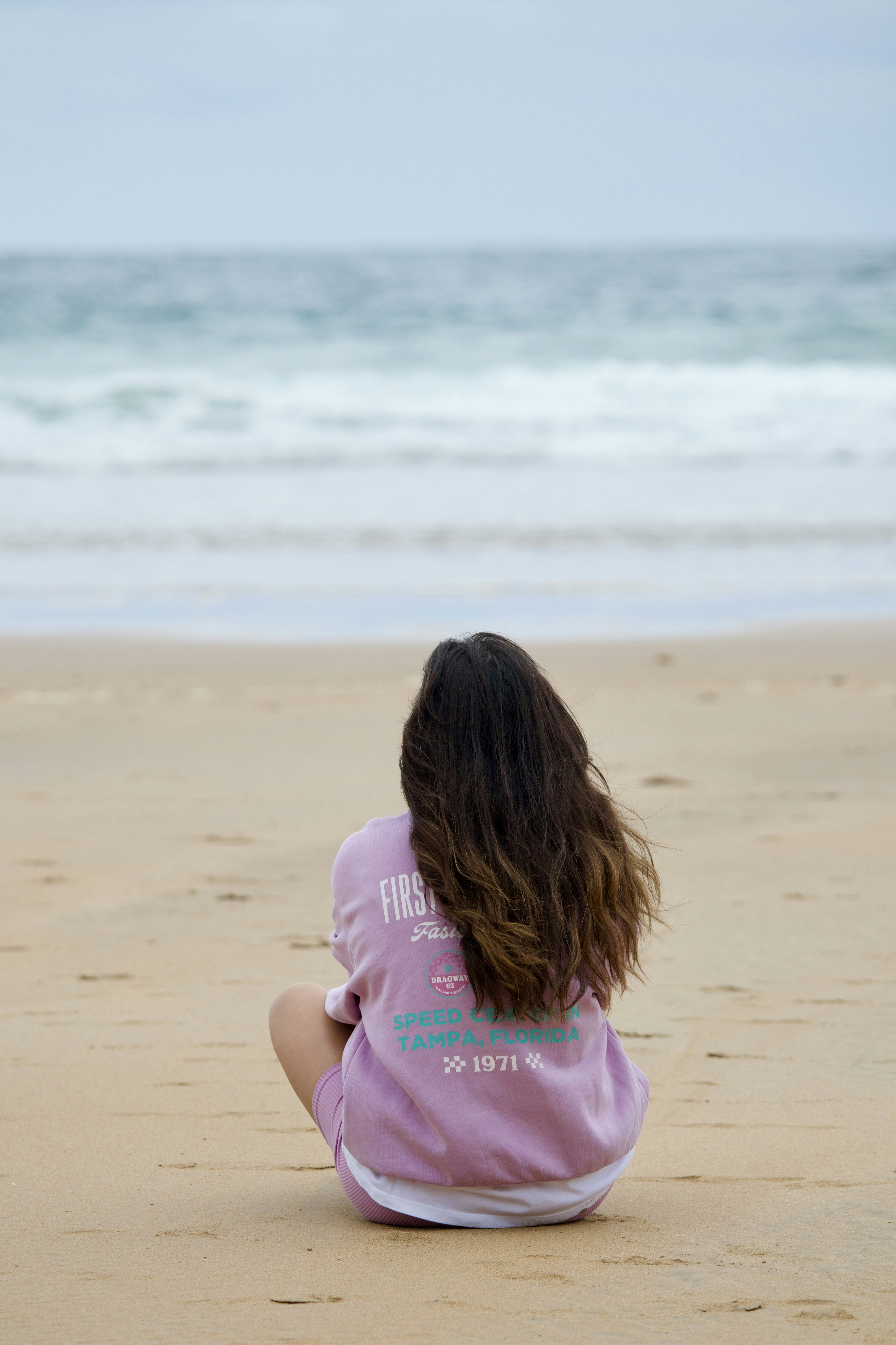 Una chica sentada en la playa mirando el océano