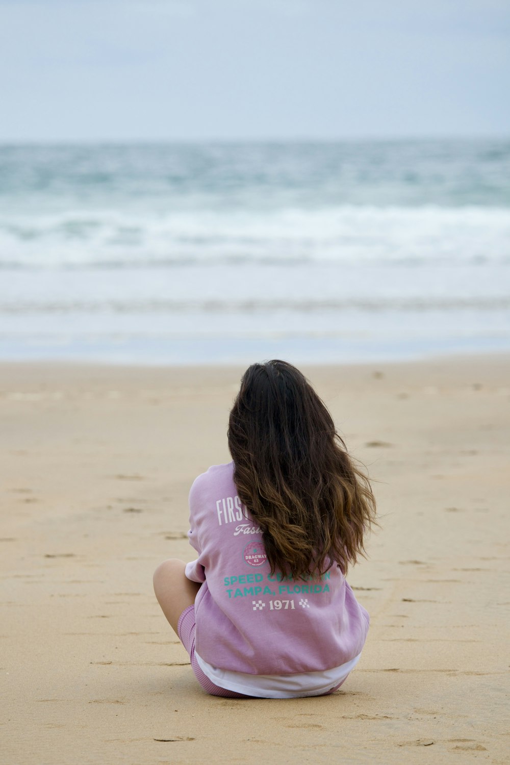 a girl sitting on the beach looking at the ocean