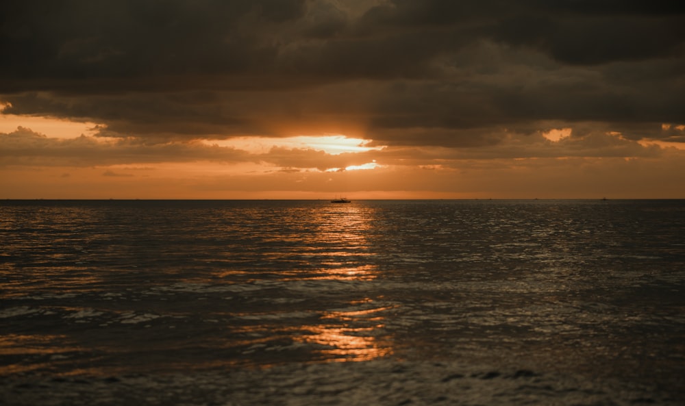 the sun is setting over the ocean on a cloudy day