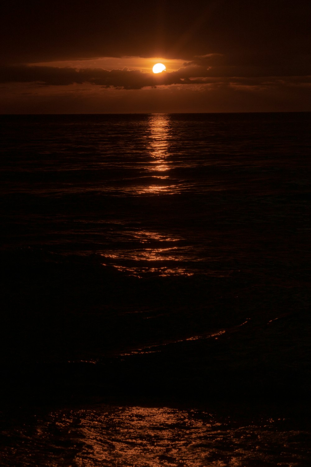 the sun is setting over the ocean on a cloudy day