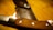 A close-up view of a finely crafted knife with a wooden handle lying beside a leather sheath, which has the brand name and logo embossed on it. The blade appears sharp and well-polished, and the leather is stitched with precision.