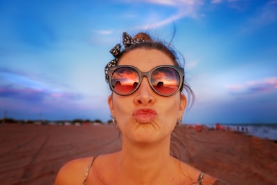 Close-up of a woman applying bright summer lipstick with the ocean in the background