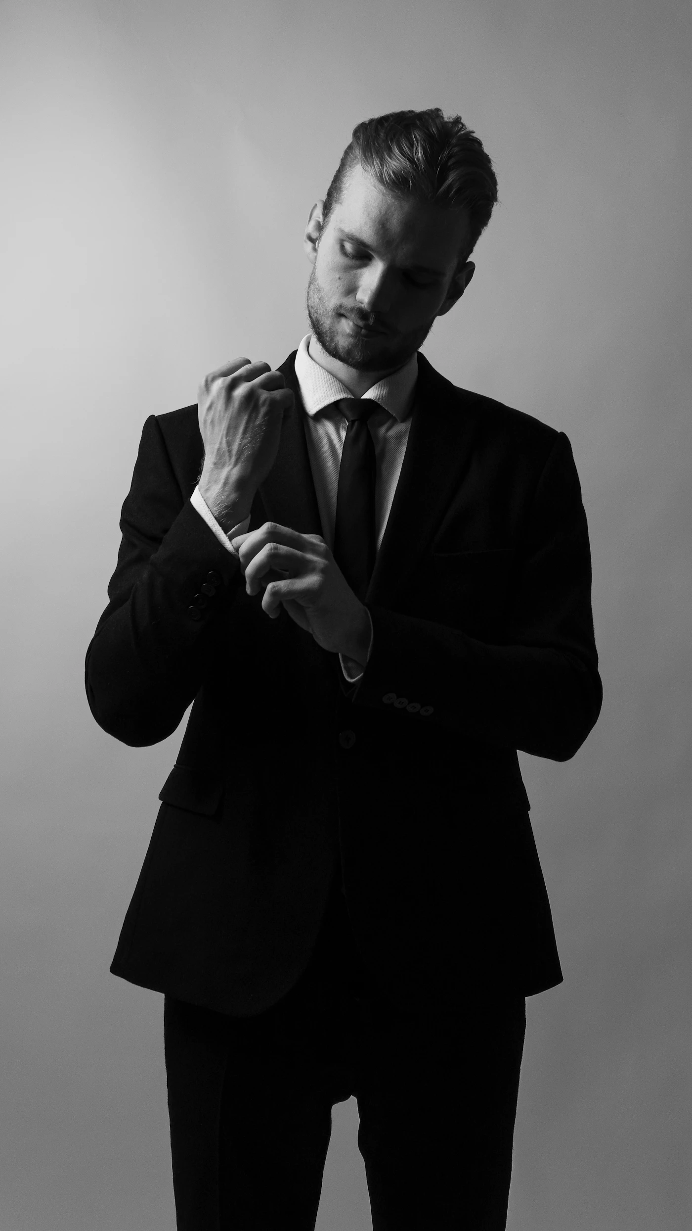 A sharply dressed man in a dark suit adjusting his cufflink