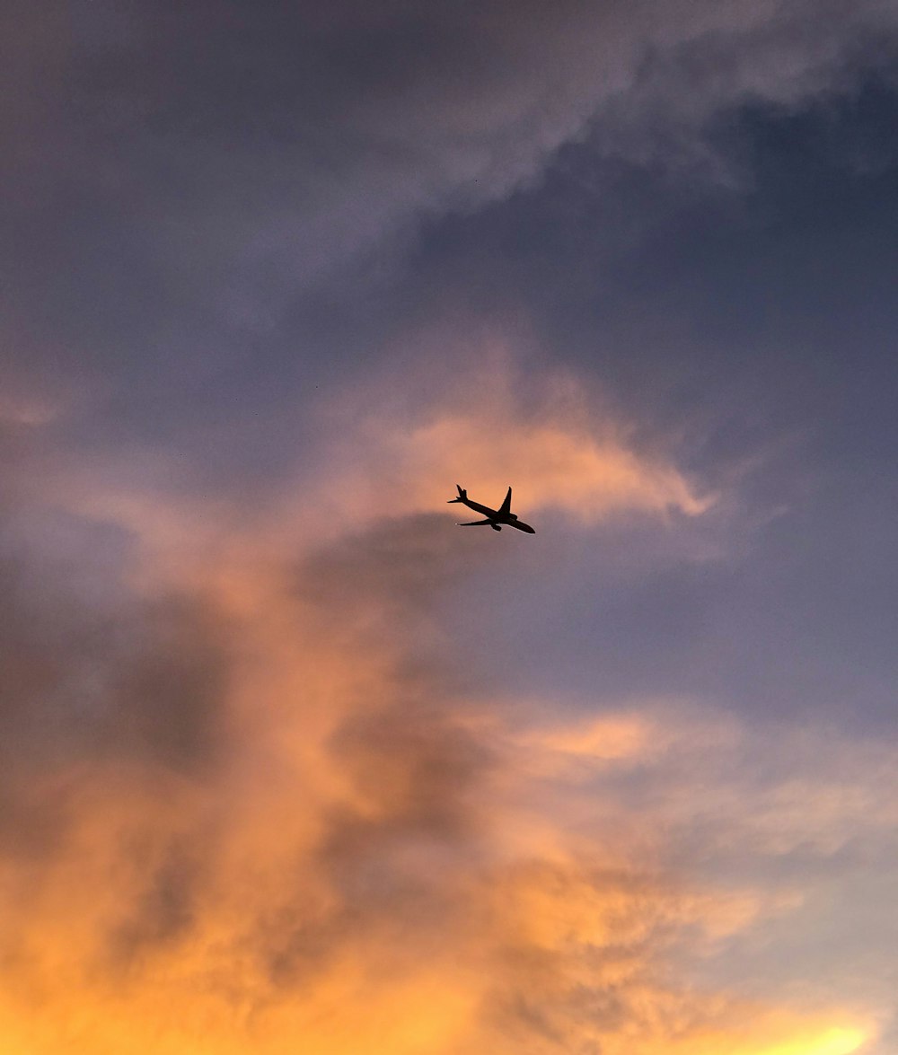 a plane flying through a cloudy sky at sunset