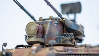 A detailed model of a military tank featuring a camouflage pattern and various mounted components, including antennas and a radar system. The tank is adorned with a distinct emblem on its turret.