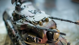 A detailed model tank with camouflage colors and intricate design, featuring dual long-barrel cannons and various surface textures details.