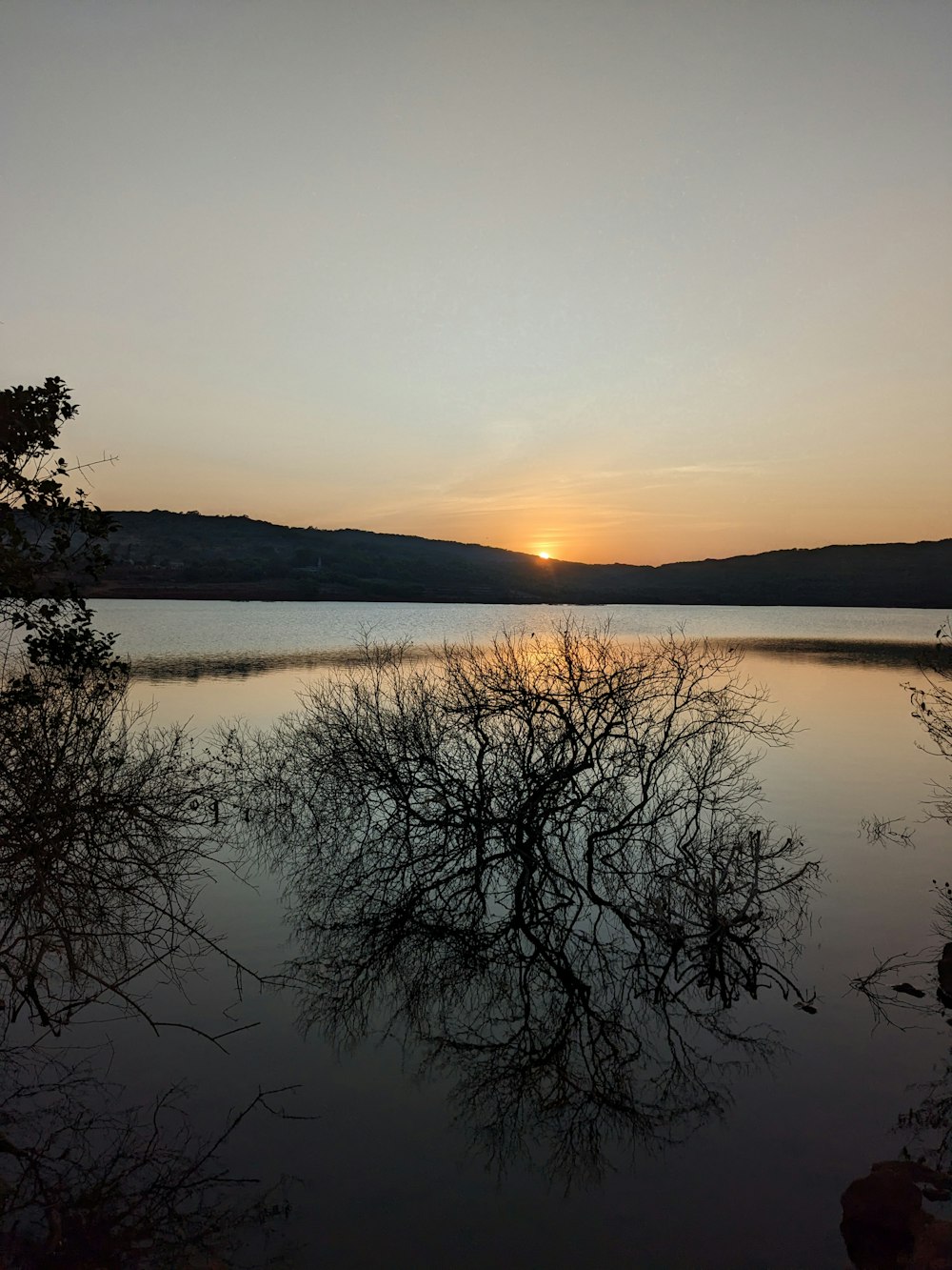 the sun is setting over a lake with trees in the foreground