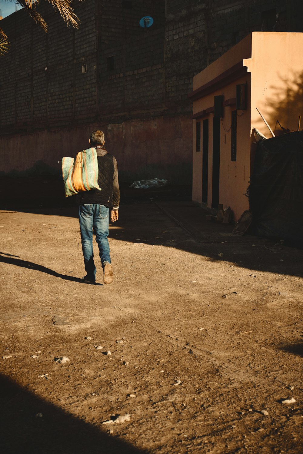 a man walking down a dirt road carrying a surfboard