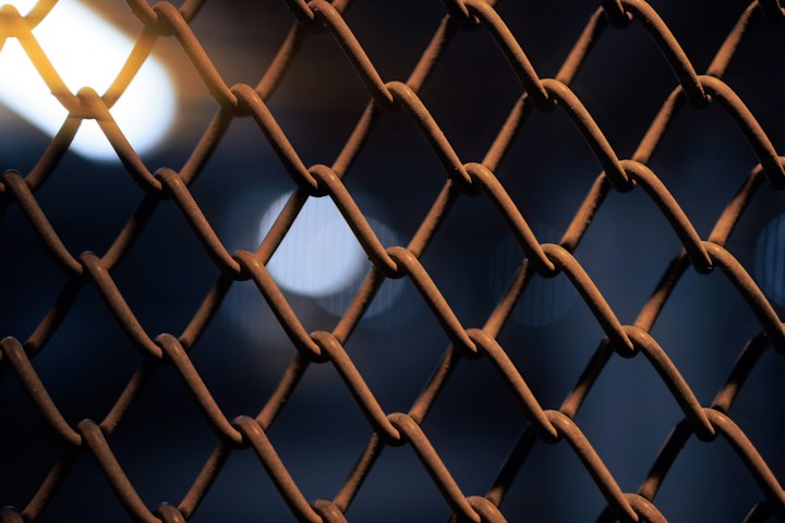 Close-up of a rusted chain link fence against a dark background
