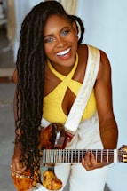A young woman smiling while holding a guitar, sitting in a cozy music studio.