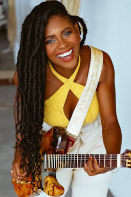 A young woman smiling while holding a guitar, sitting in a cozy music studio.