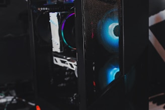 A sleek gaming computer case with visible internal components. The case features RGB lighting with a prominent blue hue emanating from the fans. The mesh panel in front allows a glimpse of the glowing interior, highlighting the modern hardware inside.