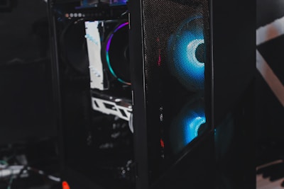 A sleek gaming computer case with visible internal components. The case features RGB lighting with a prominent blue hue emanating from the fans. The mesh panel in front allows a glimpse of the glowing interior, highlighting the modern hardware inside.