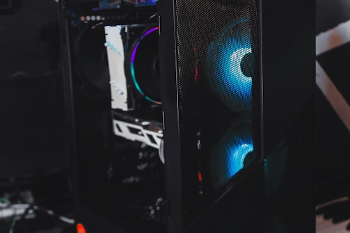 A sleek gaming computer case with visible internal components. The case features RGB lighting with a prominent blue hue emanating from the fans. The mesh panel in front allows a glimpse of the glowing interior, highlighting the modern hardware inside.