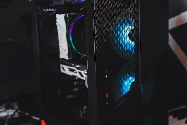 A sleek gaming computer case with visible internal components. The case features RGB lighting with a prominent blue hue emanating from the fans. The mesh panel in front allows a glimpse of the glowing interior, highlighting the modern hardware inside.