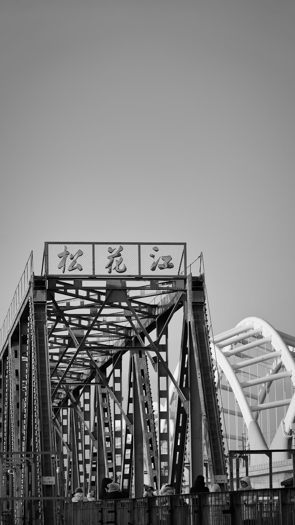 a black and white photo of a bridge with a roller coaster in the background