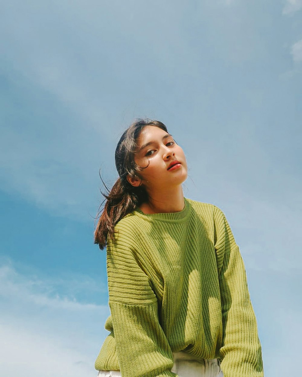 a girl in a green sweater looking up at the sky
