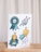 A set of colorful illustrations on a card, including a blue rosette with the word 'feey', a trophy with leaves at the base, a cartoon character with a blue hat holding a '#1' foam finger, and the phrase 'absolut philodentastisch' with decorative leaves.