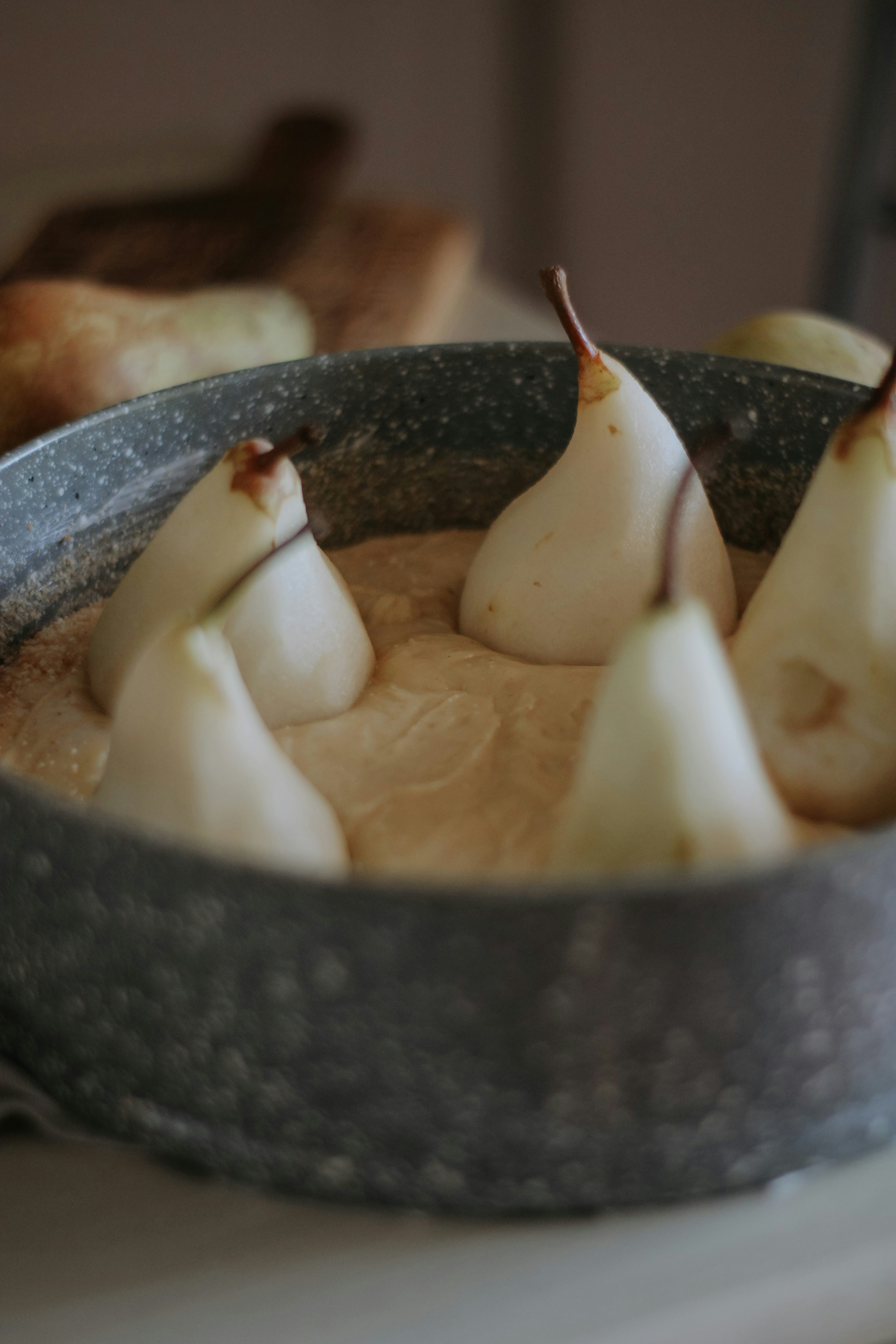 Poached pears in creamy sauce served in a dark ceramic bowl with spoon