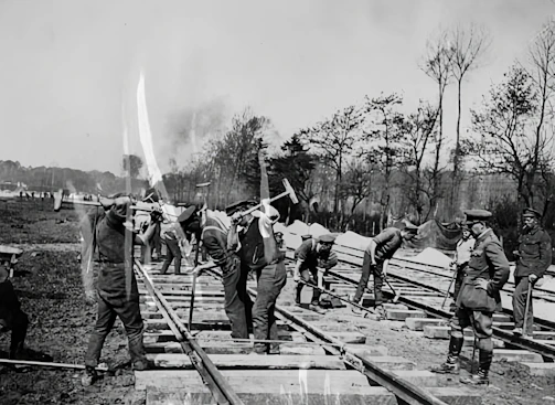 Close-up of engineers discussing plans beside railway tracks with French and Moroccan flags in the background.
