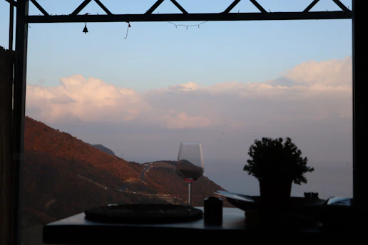 A runner pausing on a vineyard trail at sunset, holding a glass of red wine with rolling hills in the background.