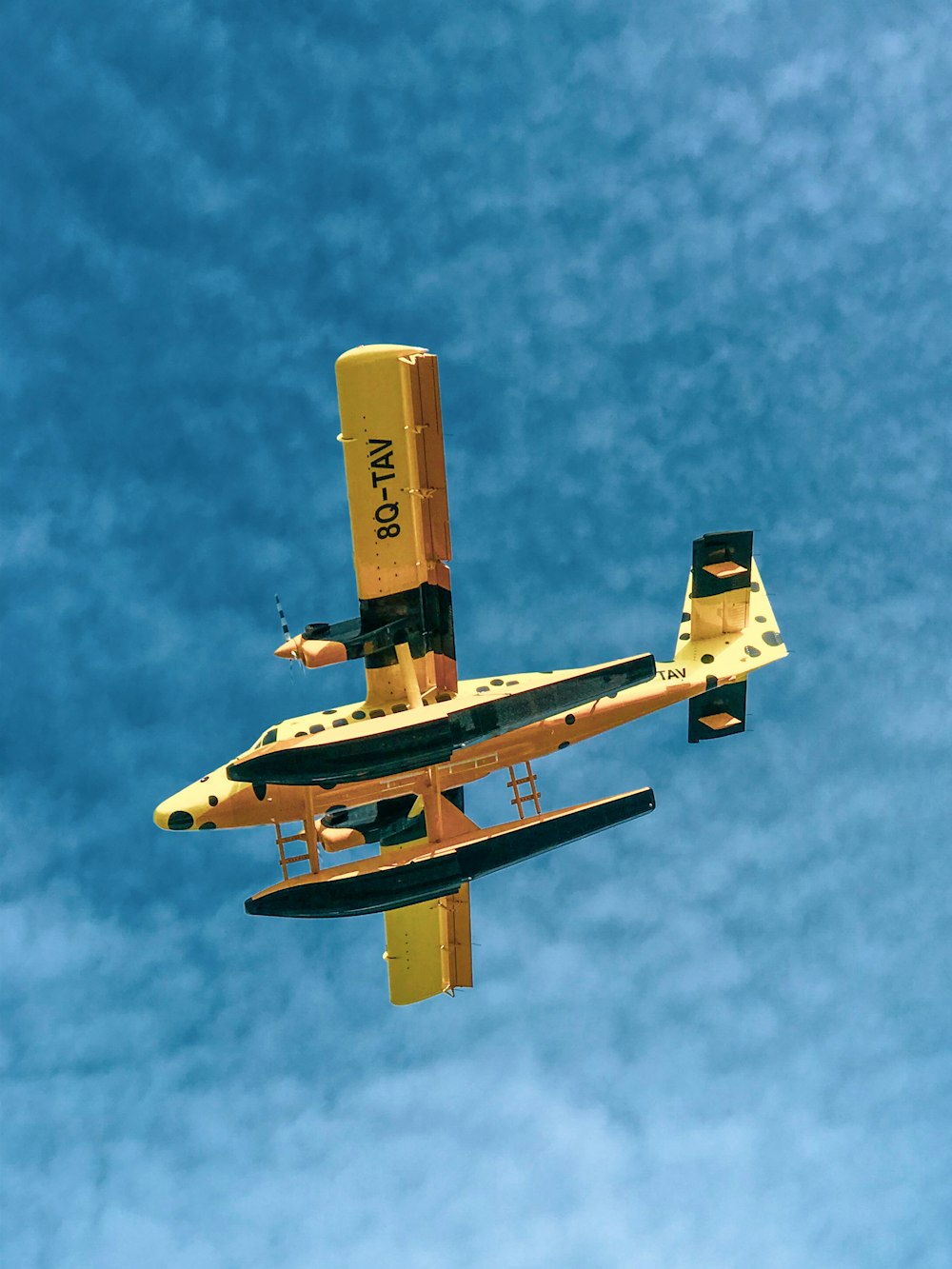 a small yellow airplane flying through a blue sky